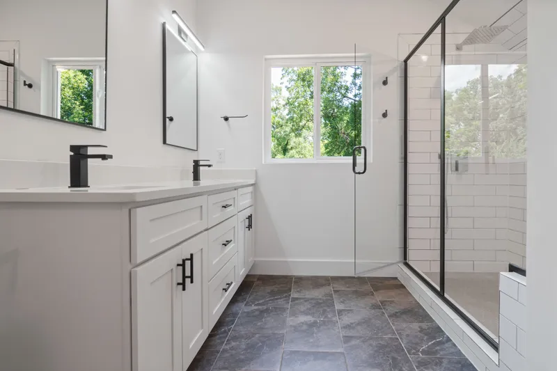 A finished bathroom shows a double vanity, dark fixtures, a glass shower enclosure, and white subway wall tile.