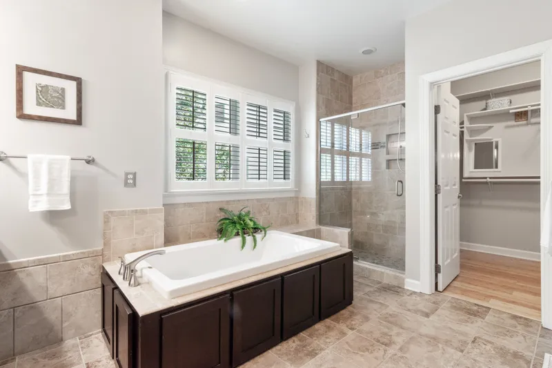 A finished bathroom has a tub with a tiled surround, a separate glass shower, and tile flooring leading to a closet.