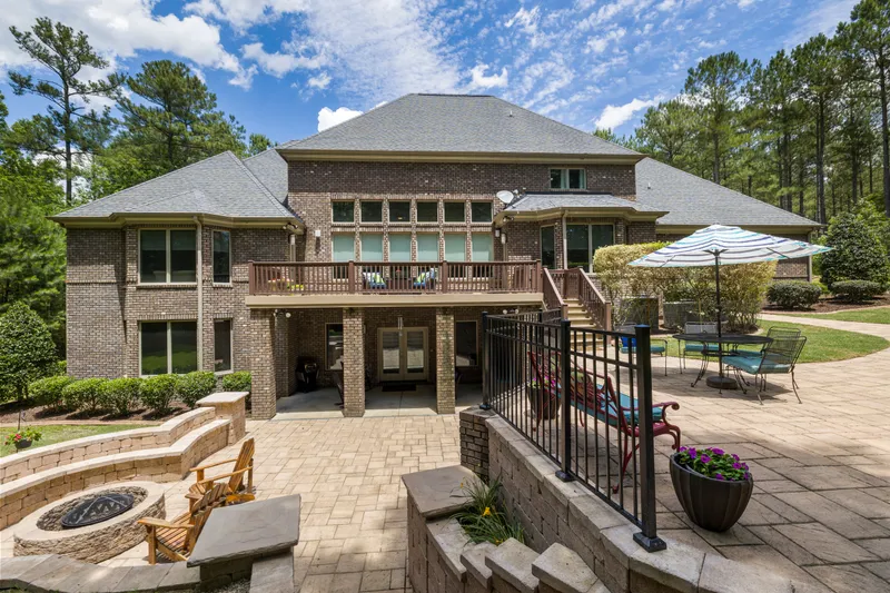 A finished brick house has an elevated deck, exterior stairs, and a paver patio with a masonry fire pit.