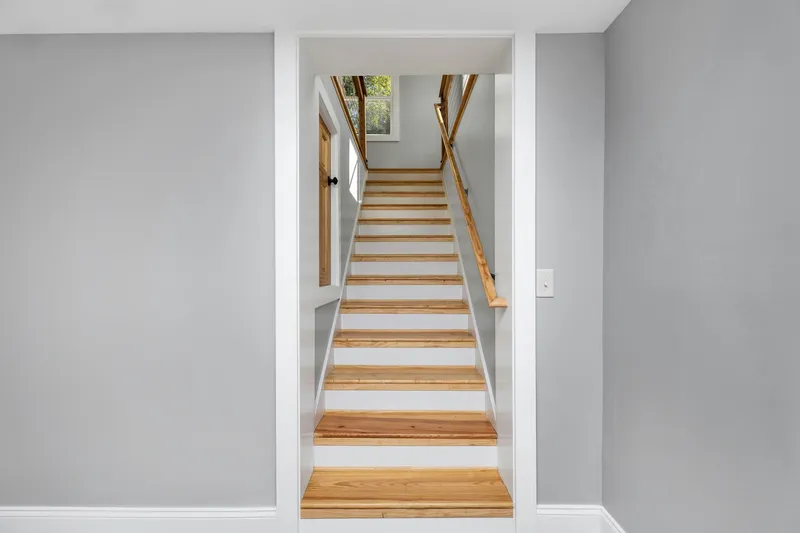 Wood stair treads, white risers, wall trim, and a wood handrail complete a straight residential stair.