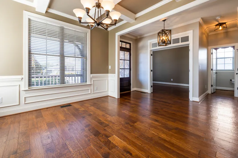 A finished room shows a coffered ceiling, paneled wainscoting, wide window trim, and wood flooring.