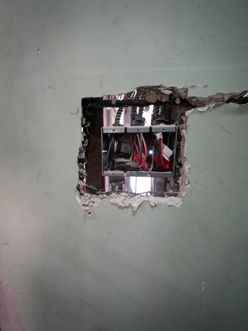 Open electrical boxes and conductors are exposed in a wall opening during interior renovation.
