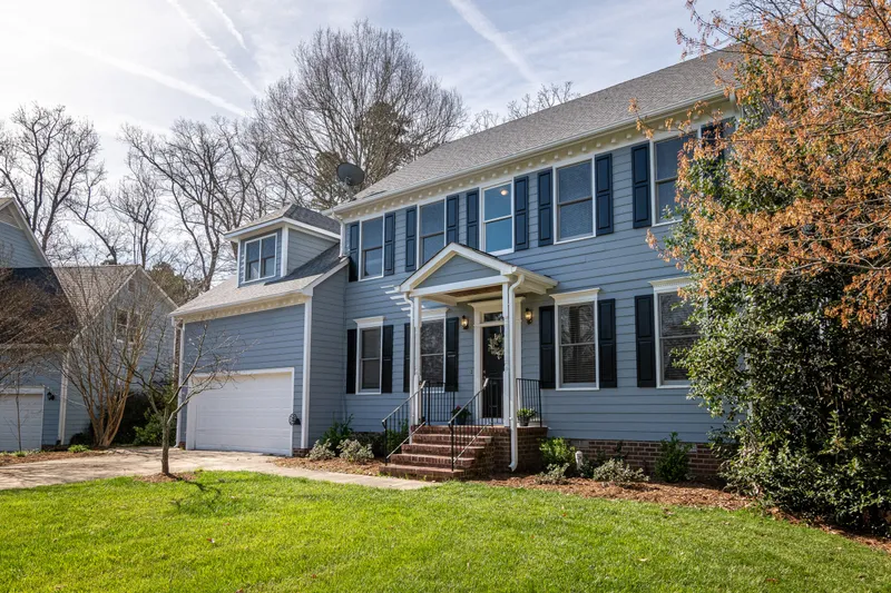 A completed two-story home shows lap siding, window trim, porch columns, brick steps, and a shingled roof.