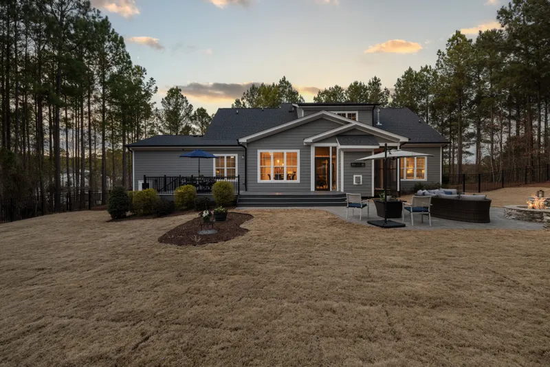 A finished rear elevation at dusk shows lap siding, large windows, deck steps, and an outdoor seating area.