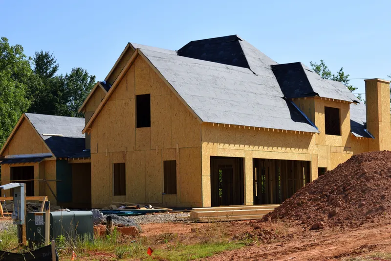 House under construction with plywood wall sheathing, open window rough openings, and roof underlayment.