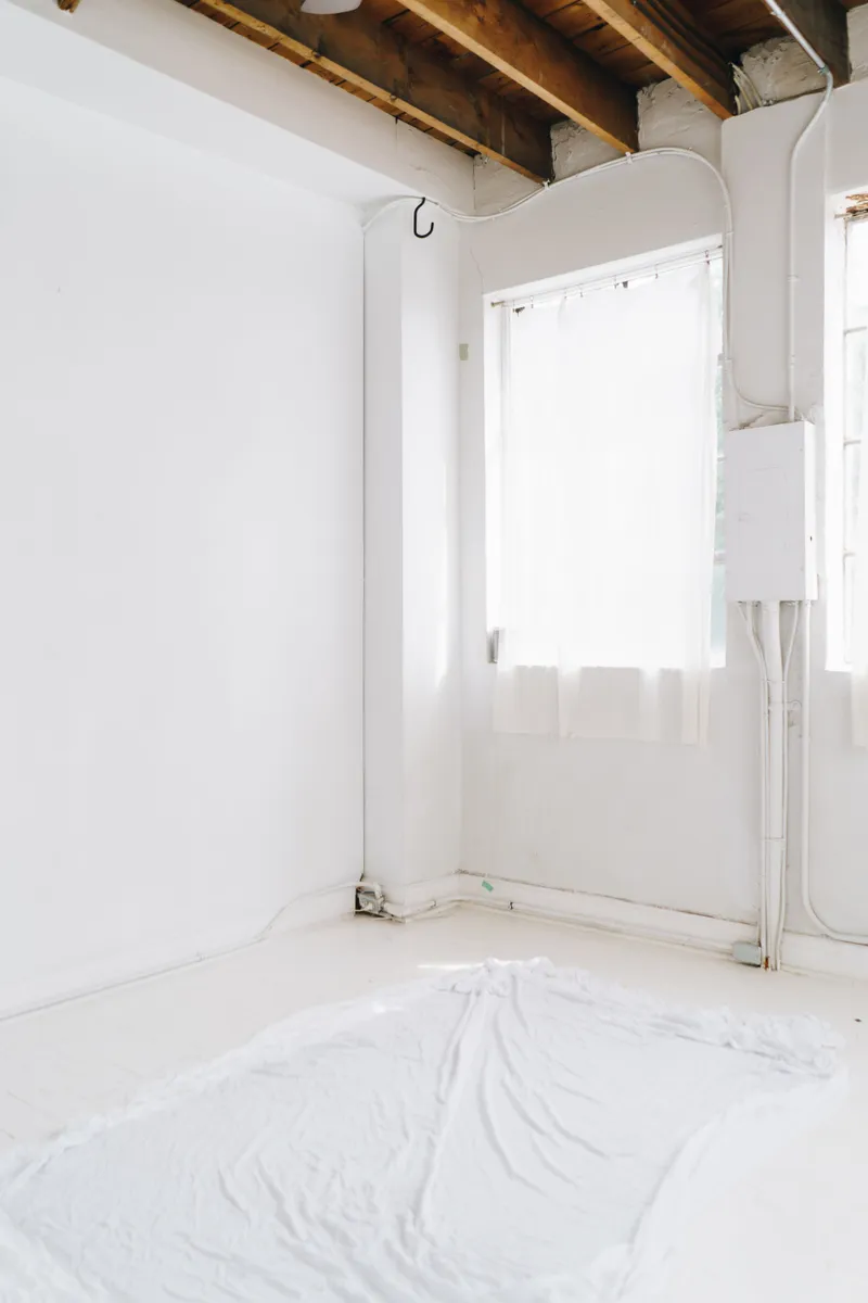 A bright room has prepared white walls, exposed wood ceiling joists, and floor protection for finish work.