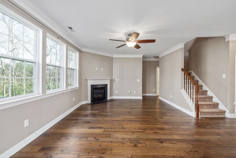 Wood flooring runs past a trimmed fireplace and a carpeted stair with wood handrail and white balusters.