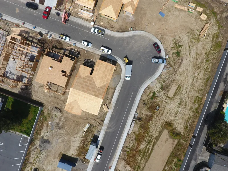 An aerial view shows homes at framing and roof-sheathing stages along a curved subdivision street.