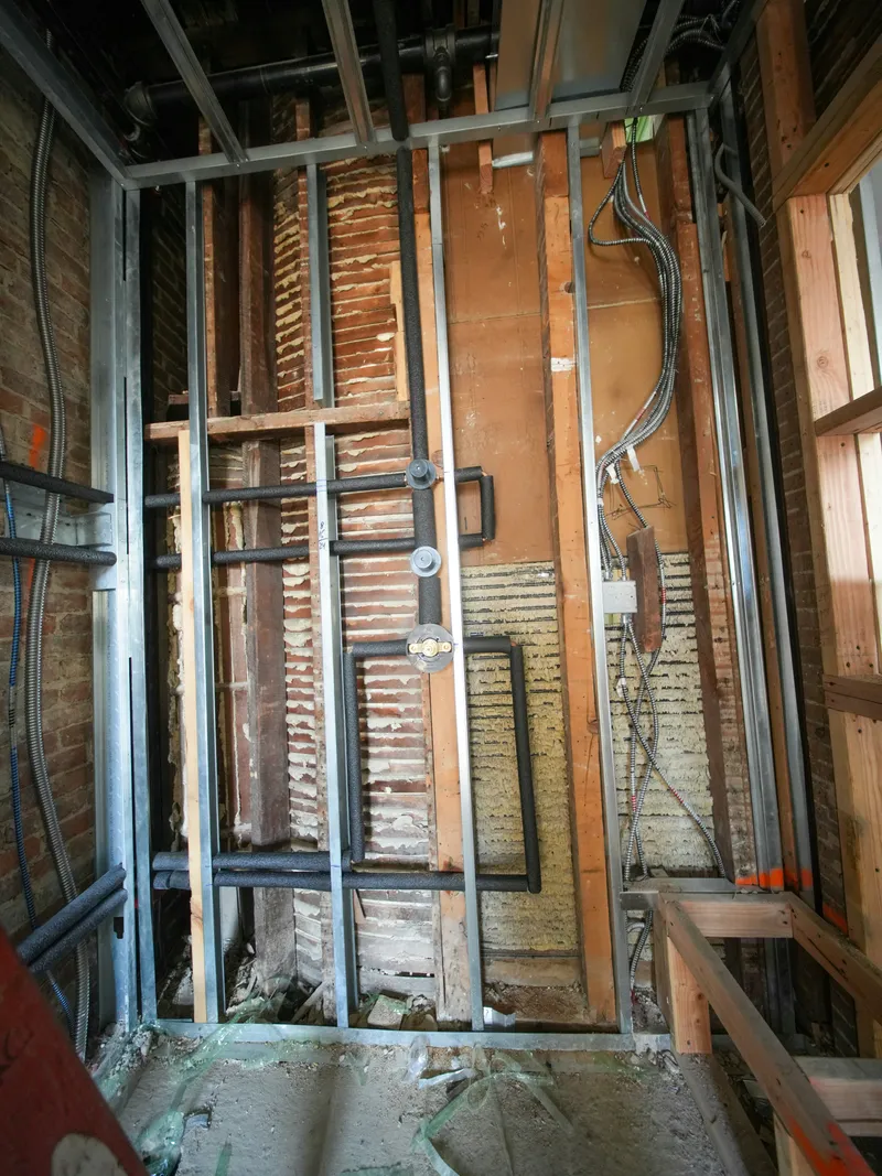 Insulated plumbing lines and flexible electrical conduit run through open wall framing during a home renovation.