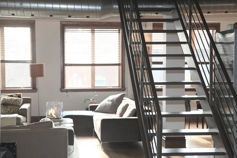 Exposed round HVAC ductwork runs above the windows and metal stair in a finished residential loft.