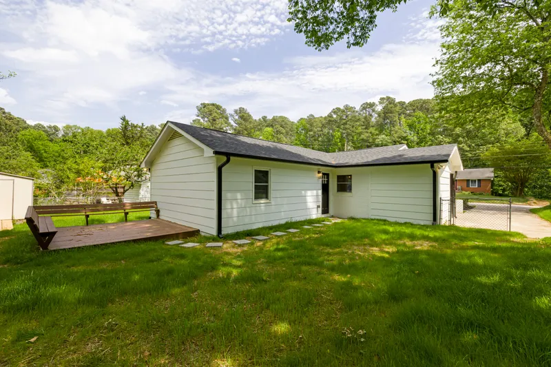 A single-story rear elevation shows light lap siding, dark gutters, a shingled roof, and a low wood deck.