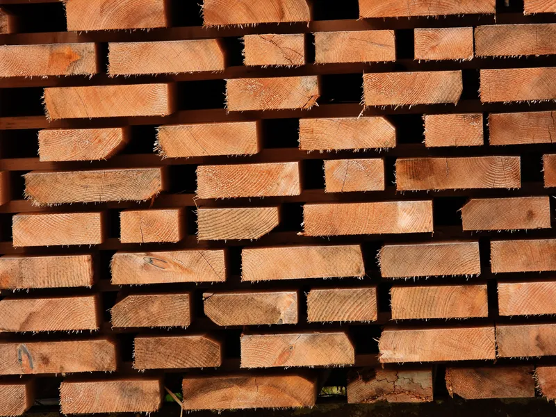 Freshly cut lumber is stacked in horizontal courses with board ends exposed to sunlight.