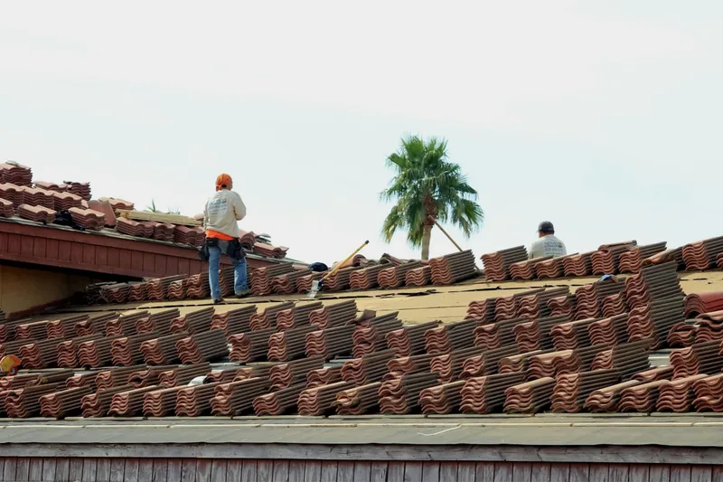 Roofers work across a pitched roof with stacks of terracotta tiles ready for installation.