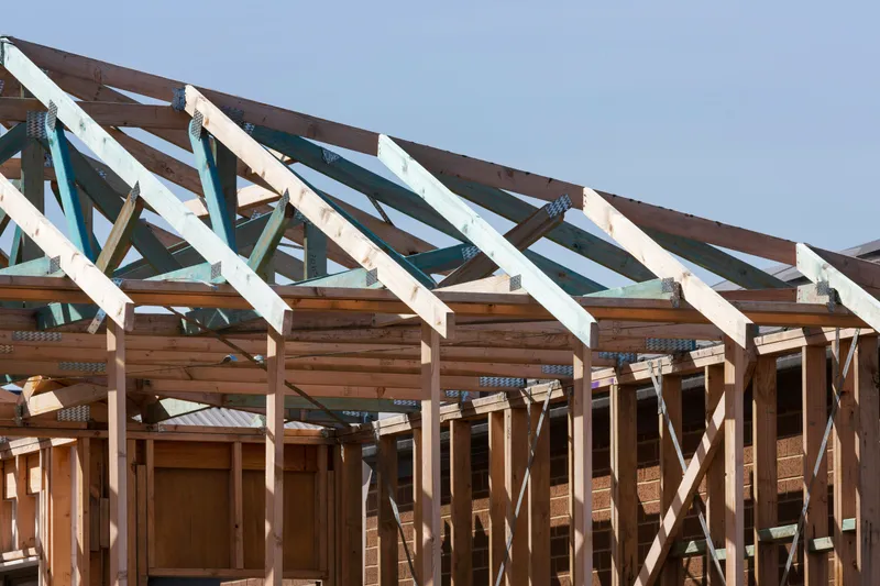 Installed timber roof trusses with metal connector plates above unfinished wall framing.