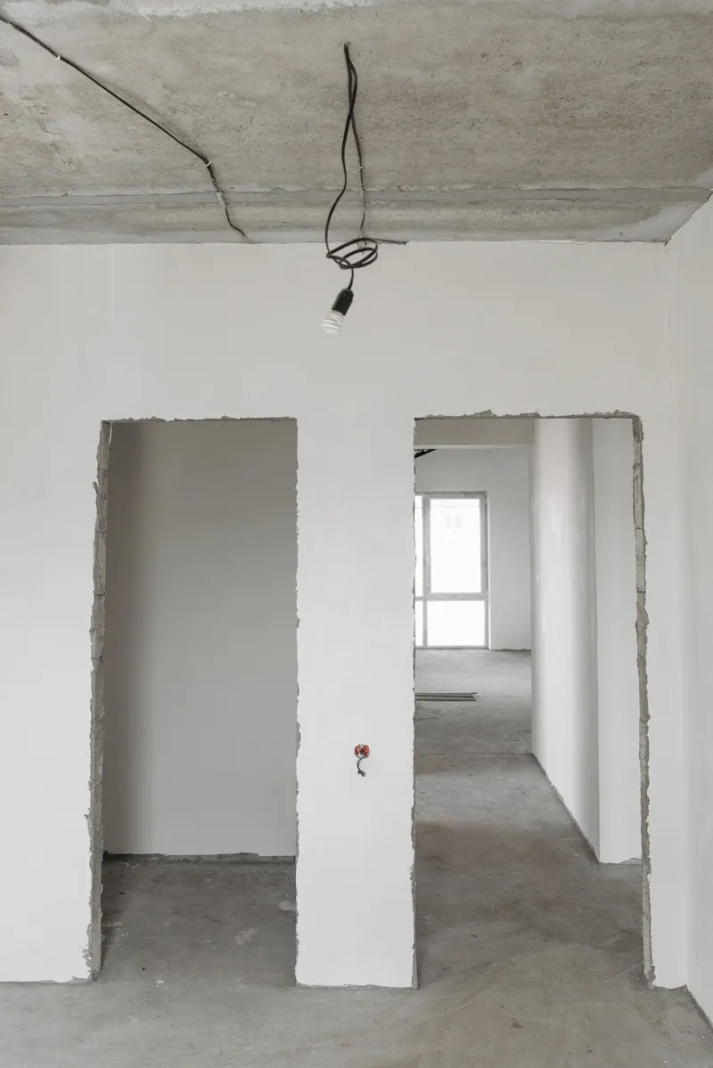 Untrimmed interior door openings and finished white wall surfaces sit below an exposed ceiling and hanging wiring.