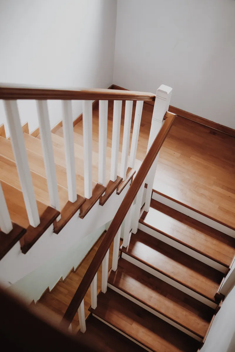 A finished wood stair has white risers and balusters with a wood handrail at the landing.